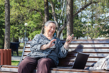 Fototapeta premium Attractive senior woman sitting on bench using smartphone and computer for remote online chat.