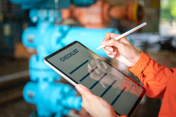 Action of a human is using digital pen to perform checklist on tablet with background of factory workplace. Industrial and technology working concept. Close-up and selective focus at hand's part. - obrazy, fototapety, plakaty