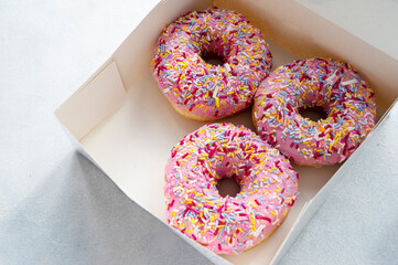 Pink donut with sprinkles on bright background in paper box