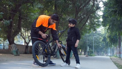 A young Indian father helping his young son to fix a bike - fixing bicycle fatherhood parenting growing kids . A little boy spending time with his father in a public park - parenting father-son...