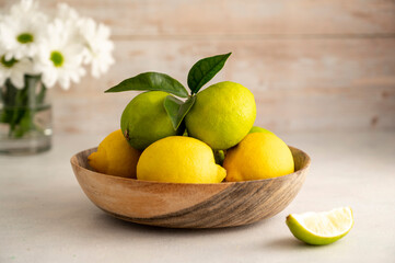 Bowl with fresh limes and lemons, on wooden background. Fresh citrus fruits with fresh flowers
