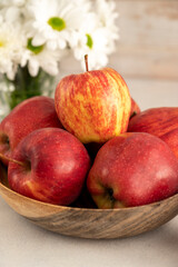 Red apples in bowl on wooden rustic background. Fresh red apple fruits with flowers.