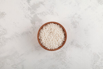 White sago pearls or tapioca pearl in wooden bowl on light textured background, top view
