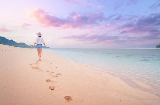 Vacation on the seashore. Back view of young woman walking away on the beautiful tropical white sand beach.