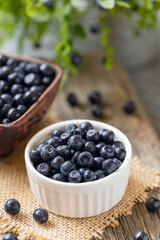 Fototapeta na wymiar Wild blueberries in white bowl on burlap on wooden table. Natural superfood with vitamins.