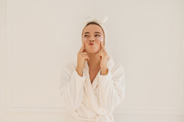 Funny young caucasian girl grimaces looking away touching her cheeks on white background. Pretty...