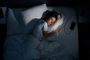 Young woman hugging pillow in bed, top view.