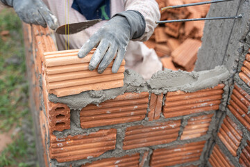 Construction worker installing bricks masonry bricklayer and adjusting bricks walls using trowel, mortar and putty knife.