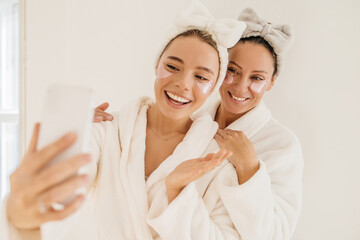 Pretty caucasian young ladies wear patches under their eyes for cleaning and take selfie on...