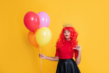 surprised child in crown with party balloon on yellow background