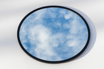 A round or oval mirror with a reflection of the blue sky and white clouds. Close-up. Isolated on a white background