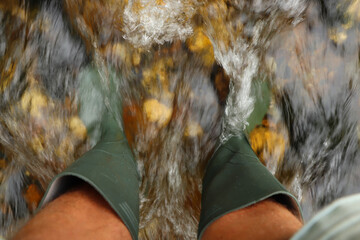 Fast flowing water crashing over green wellies in a river in South Cornwall