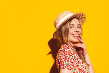 Portrait of young beautiful smiling blond female in trendy summer clothes. carefree woman posing near yellow wall in studio. Positive model having fun indoors. Cheerful and happy. In hat