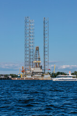 A tourist or excursion ship sails in the waters of the Gulf of Finland against the background of a drilling rig in Kronstadt, Petrovskaya Gavan, Kotlin Island