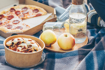 Eco paper bowl with Belgian waffle, pepperoni pizza, apples and bottle with water on picnic plaid