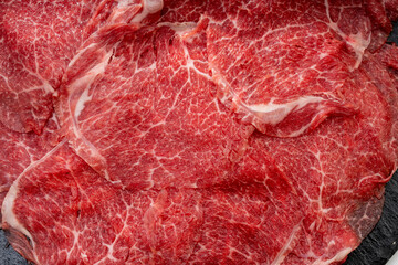 Close up shot Rare Sliced Wagyu beef with marbled texture on black plate, Meat red beef on wooden background, Asian shabu shabu Sukiyaki food style.