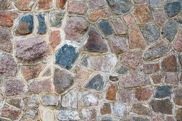 A close-up of the stone wall. The texture of masonry is made of multi-colored stones connected with cement mortar.