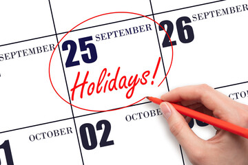 Hand drawing a red circle and writing the text Holidays on the calendar date 25 September . Important date.