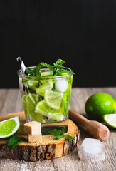 Ein Mojitto Cocktail mit frischer Pfefferminz und Limetten in einem Trinkglas auf einem Holz Tisch. Schwarzer Hintergrund, rustikaler Stil.