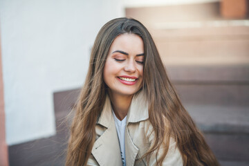 Portrait of a young beautiful long-haired woman in a European city. A model in stylish casual wear is relaxing outside.