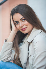 Portrait of a young beautiful long-haired woman in a European city. A model in stylish casual wear is relaxing outside.