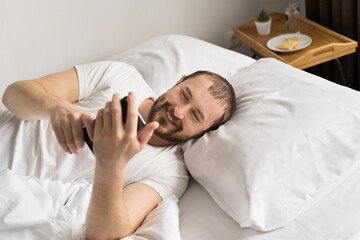 smiling man on bed  at  home interior chatting with friends and browsing the internet in the morning,  social networks concept