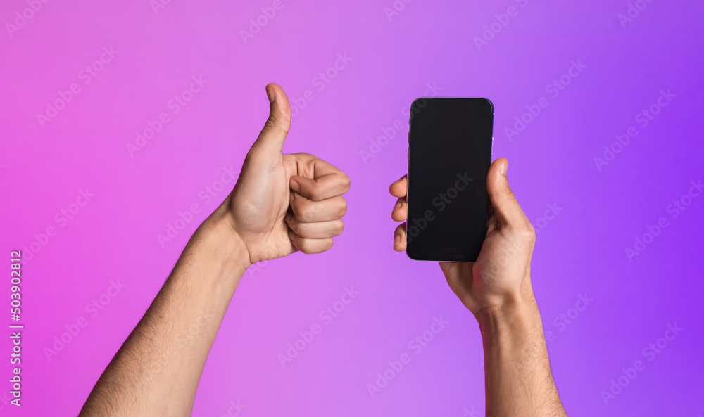 Poster Cropped view of young guy showing smartphone with empty screen and gesturing thumb up, recommending mobile app mockup