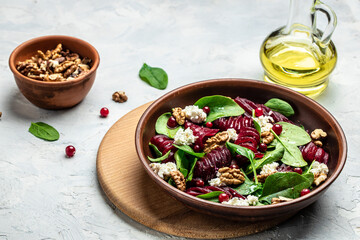 Beet or beetroot salad with baby spinach, cheese, nuts, cranberries on plate with fork, dressing and spices on light background, Food recipe background. Close up