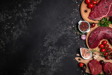 Assortment of raw cuts of raw beef meat steaks with spices on a dark background. Long banner format. top view
