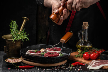 Cooking Beef medallions wrapped in bacon with rosemary and spices on grill pan by chef hands on black background. top view. place for text