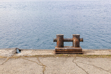 Rusty mooring bollard on the old pier, against the background of water