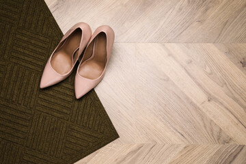 Stylish door mat and shoes on wooden floor, top view. Space for text
