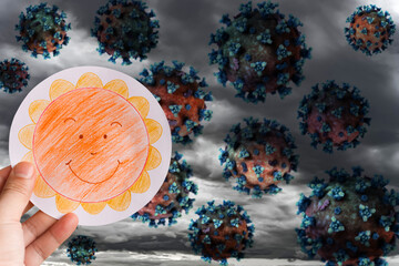 man holding picture of a smiling sun against dark clouds with horrified coronavirus concept of...
