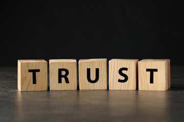 Word TRUST made with wooden cubes on grey table against black background