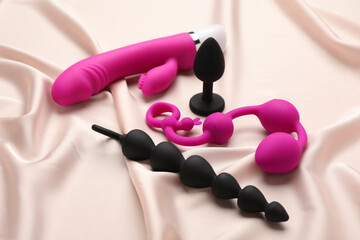 Pink and black sex toys on beige silky fabric - obrazy, fototapety, plakaty