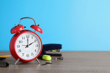 Red alarm clock and different stationery on wooden table against light blue background, space for...
