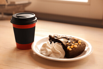 Tasty coffee in takeaway paper cup and dessert on wooden table indoors