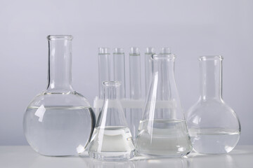 Different laboratory glassware with transparent liquid on table against light background