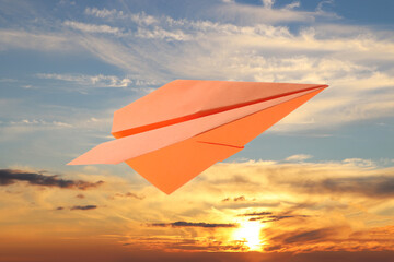 Orange paper plane and view of beautiful sky at sunset