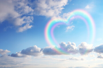 Beautiful view of heart shaped rainbow and white clouds in blue sky on sunny day
