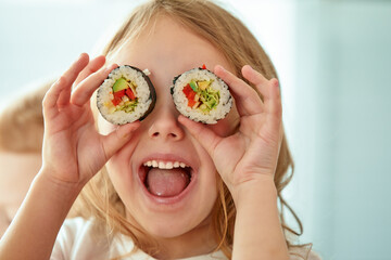 Funny little girl holding sushi rolls in front of eyes on white background