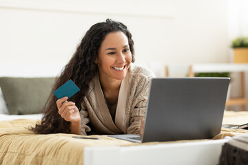 Casual smiling woman using pc and credit card at home