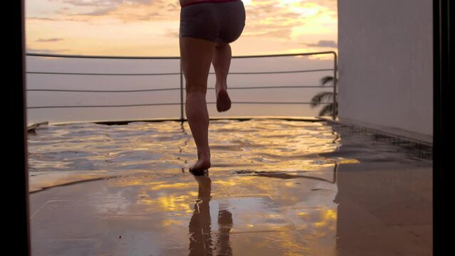 View from back of young man runs and jumps to the swimming pool splashes of water on summer vacations during sunset