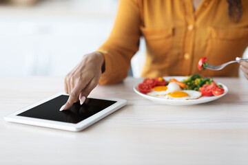 Cropped of black lady using digital tablet during breakfast