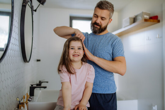 Father brushing his little daughter's hair in bathroom, morning routine concept.