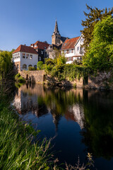 Fototapeta na wymiar Old town of Essen-Kettwig Ruhr Basin Germany reflected in water of mill ditch. The small historic village with romantic truss houses and Market Church is a tourist attraction. Blue sky in springtime.