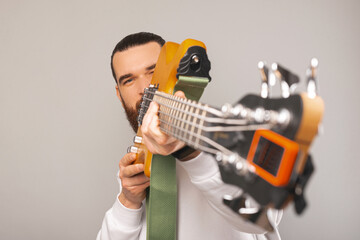 Bearded man is looking at the camera while hiding behind a bass guitar. Studio shot over grey...