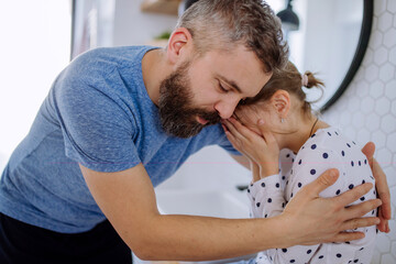 Father consoling his little upset daughter in bathroom at home.