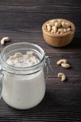 Vegetarian cream cheese made from fermented cashews in glass jar on dark wooden background.