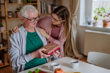 Happy woman surprising her senior father when visiting him at home and bringing present.